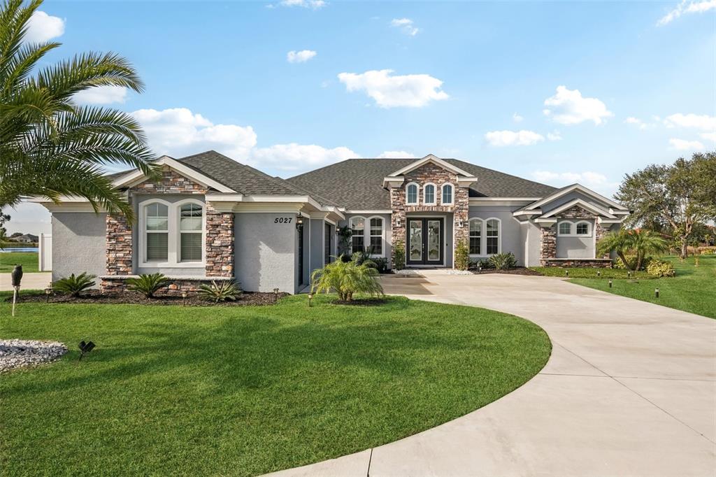 A single-story house with a gray stucco exterior, stone accents, and a curved concrete driveway — 5027 LAKE TOSCANA DRIVE, WIMAUMA, FL