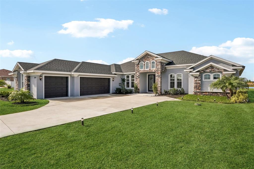 A single-story house with a gray exterior, stone accents, and a three-car garage — 5027 LAKE TOSCANA DRIVE, WIMAUMA, FL