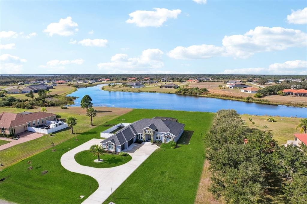 An aerial view shows a single-story house with a large lawn and a nearby lake — 5027 LAKE TOSCANA DRIVE, WIMAUMA, FL