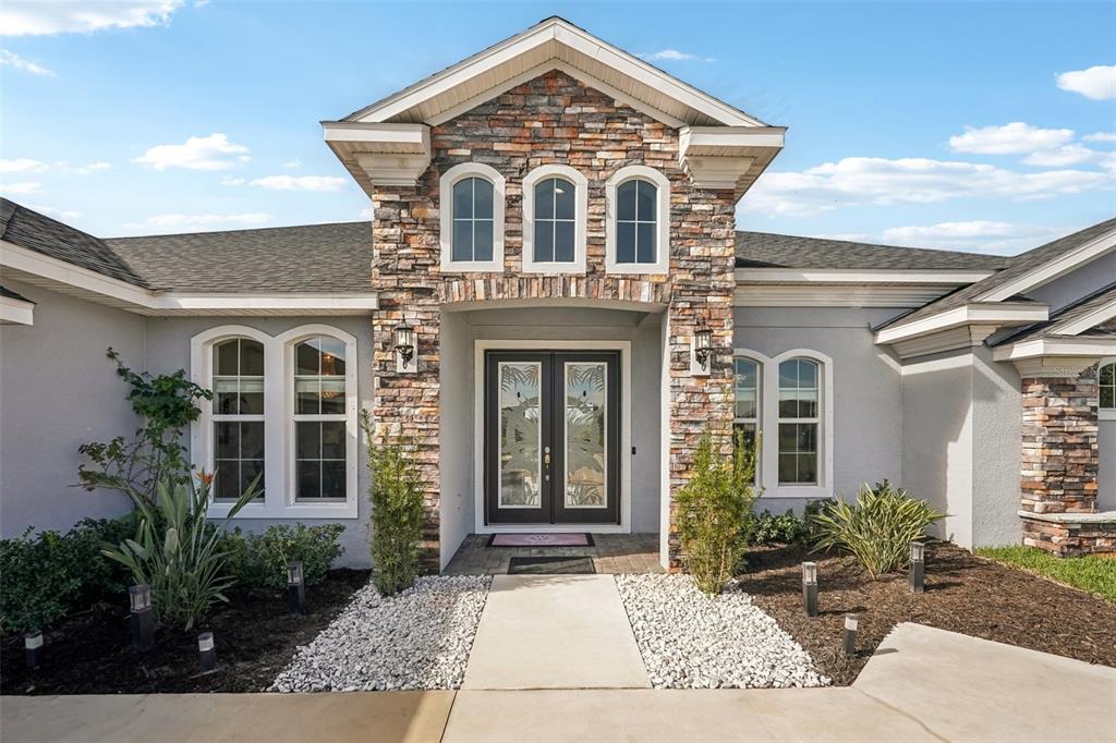 The exterior of a house features a stone facade, double front doors, and arched windows — 5027 LAKE TOSCANA DRIVE, WIMAUMA, FL