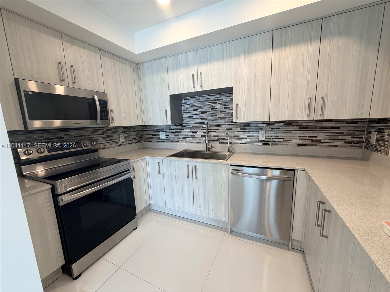 A modern kitchen features light wood-grain cabinets, stainless steel appliances, and a tiled backsplash — 10950 NW 82nd St # 416, Doral FL 33178, DORAL, FL