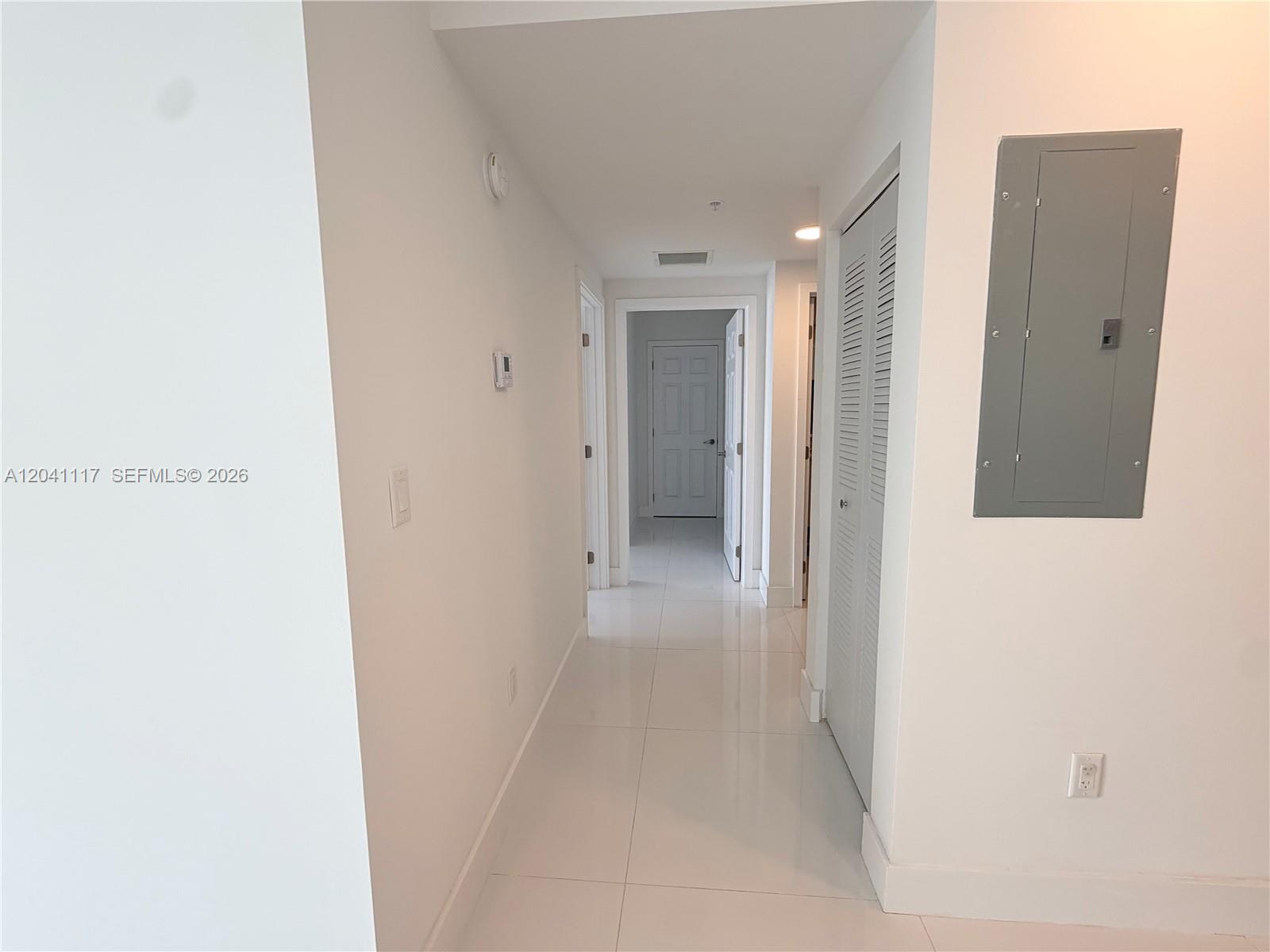 A white-walled hallway features light-colored tile flooring, a gray electrical panel, and multiple doorways — 10950 NW 82nd St # 416, Doral FL 33178, DORAL, FL