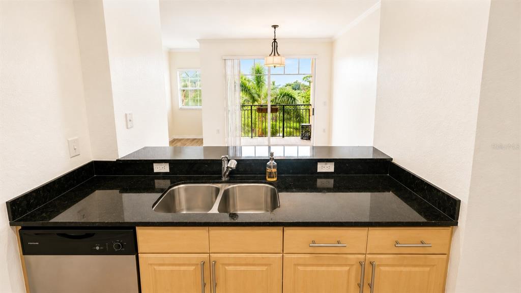 A kitchen sink with black countertops overlooks a balcony through a sliding glass door — 1064 N TAMIAMI TRAIL UNIT 1325, SARASOTA, FL