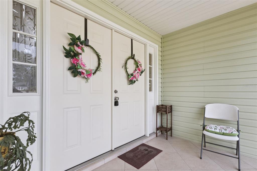 A covered porch features light green siding, a double door with floral wreaths, and seating — 5540 HAMLIN COURT, LEESBURG, FL