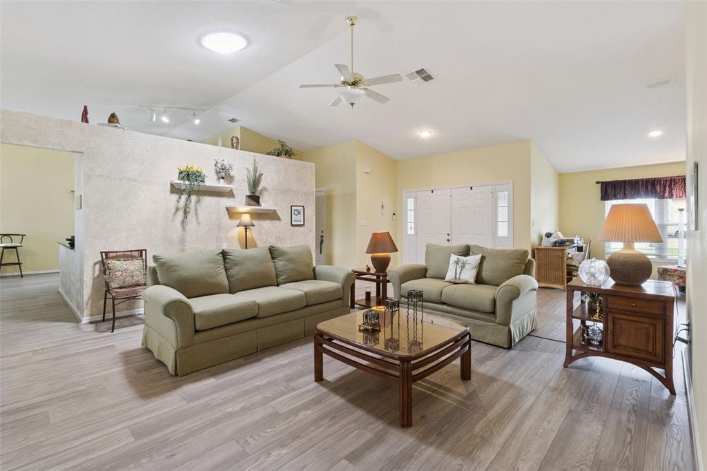 A living room features light wood-look flooring, two green sofas, and a central coffee table — 5540 HAMLIN COURT, LEESBURG, FL