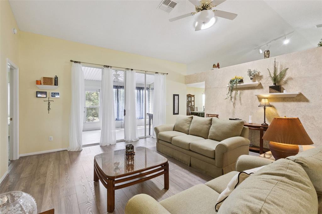 A living room features light-colored walls, wood-look flooring, a beige sofa, and sliding glass doors — 5540 HAMLIN COURT, LEESBURG, FL