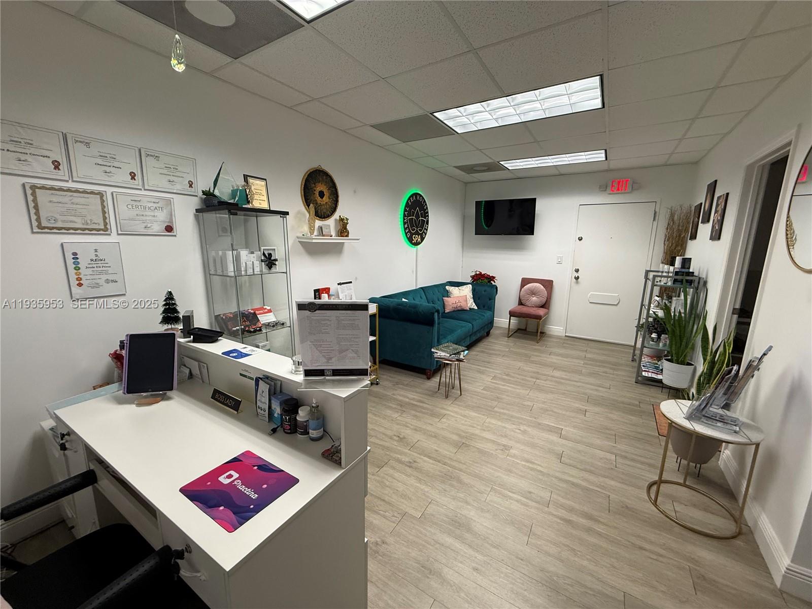 A reception area features a white desk, teal sofa, wood-look flooring, and wall-mounted certificates — 717 Ponce De Leon Blvd # 206, Coral Gables FL 33134, CORAL GABLES, FL