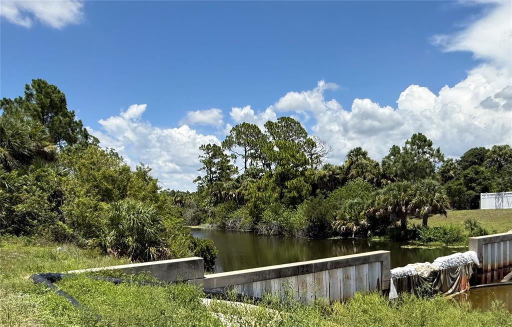 A concrete drainage structure sits in front of a pond surrounded by trees and vegetation — 3500 W PRICE BOULEVARD, NORTH PORT, FL