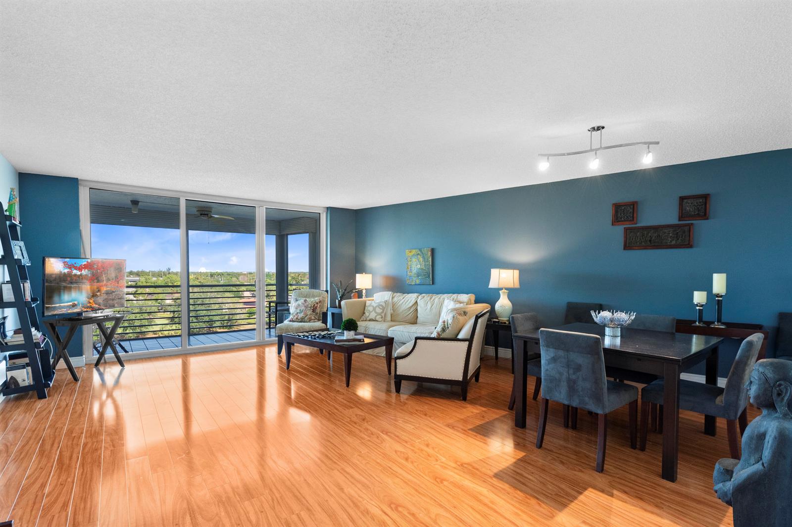 A living and dining area features blue walls, hardwood floors, and a balcony with views — 3499 Oaks Way # 806, Pompano Beach FL 33069, POMPANO BEACH, FL