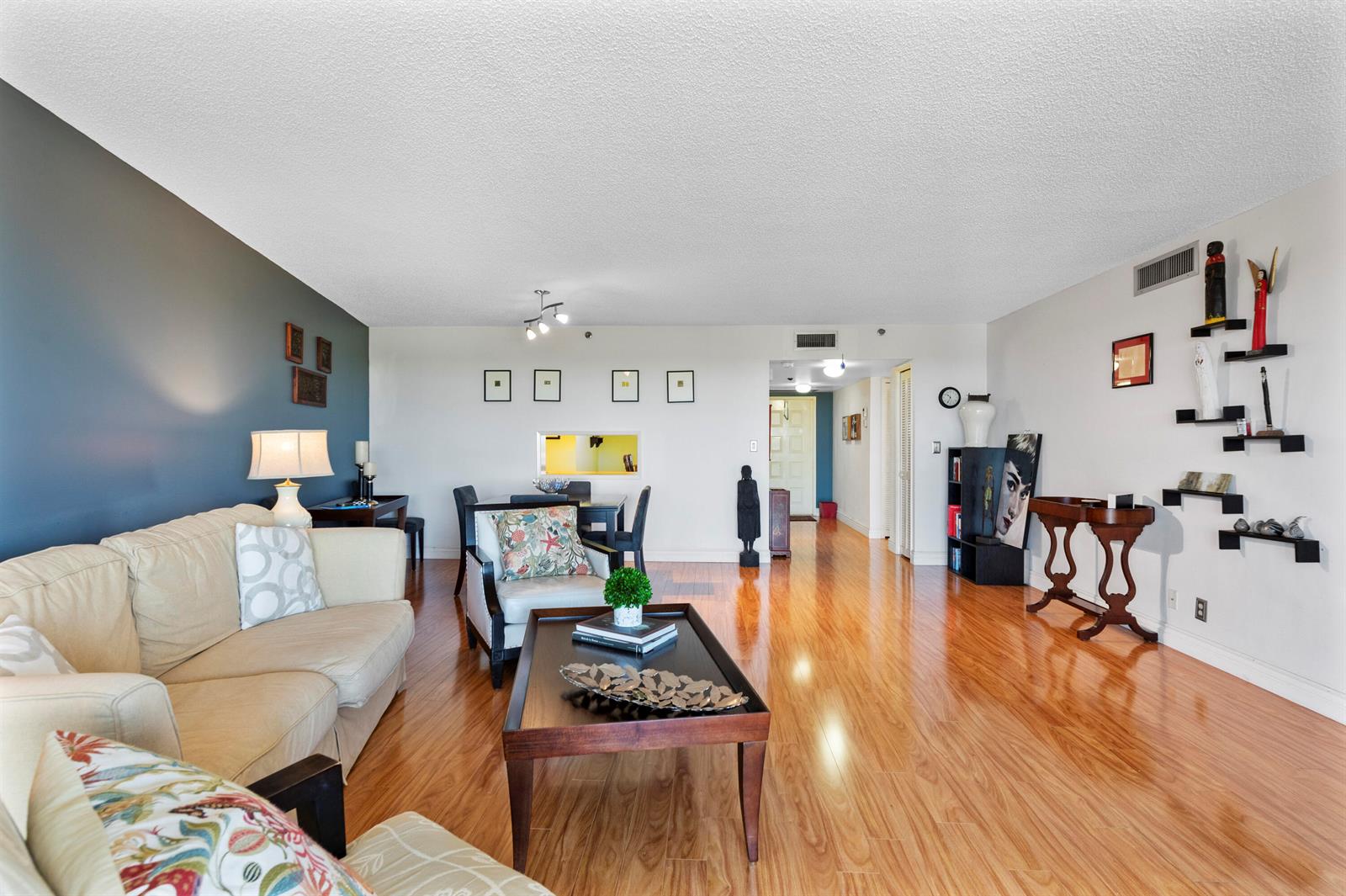 A living room with hardwood floors, a dark blue accent wall, and wall-mounted display shelves — 3499 Oaks Way # 806, Pompano Beach FL 33069, POMPANO BEACH, FL