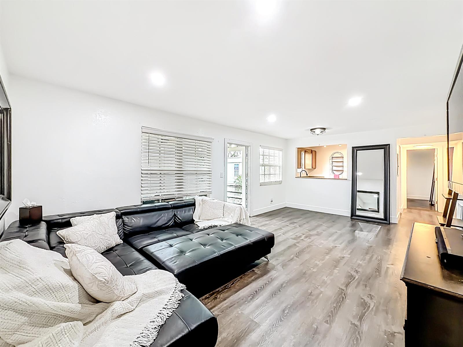 A living room features a black sectional sofa, wood-look flooring, and a pass-through kitchen window — 305 SE 11th Avenue, Pompano Beach FL 33060, POMPANO BEACH, FL