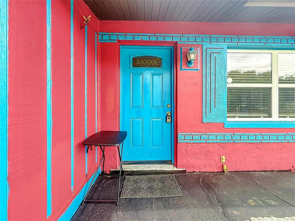 A bright pink and blue exterior wall features a matching blue front door and window — 6430 83RD AVENUE N, PINELLAS PARK, FL