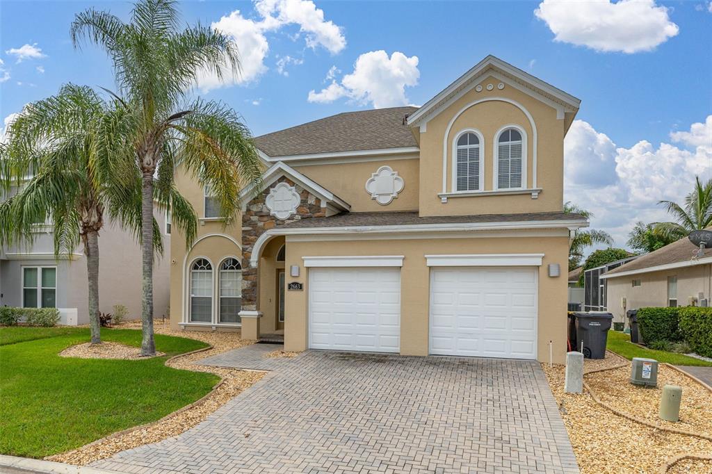 A two-story tan house with a stone accent, arched windows, and a brick paver driveway — 2663 SAND HILL POINT CIRCLE, DAVENPORT, FL
