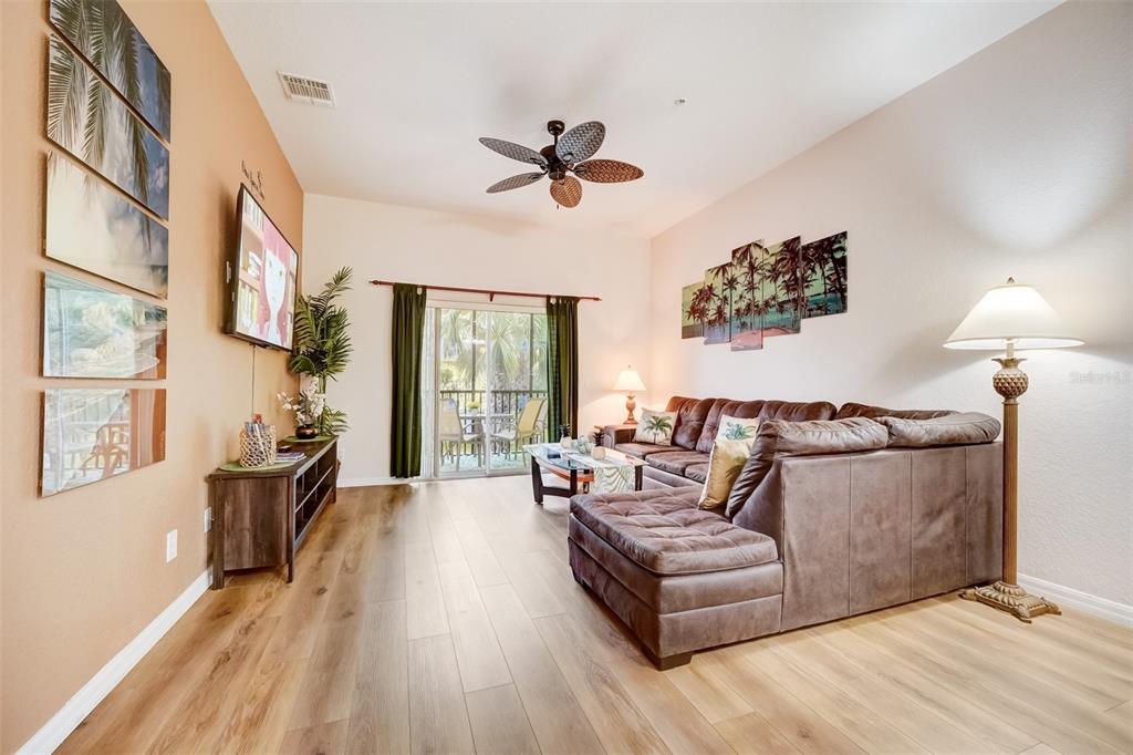A living room features wood-look flooring, a brown sectional sofa, a ceiling fan, and balcony access — 205 LUCAYA LOOP UNIT 205, DAVENPORT, FL