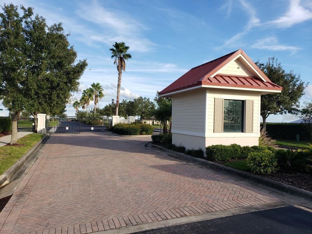 A paved driveway leads to a small guardhouse with a red metal roof — 295 SPINNAKER COURT, AUBURNDALE, FL