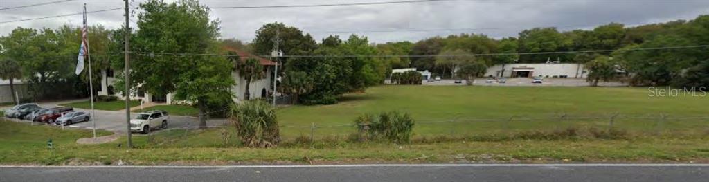 A large grassy lot sits next to a multi-story building and a parking area — 7725 N ORANGE BLOSSOM TRAIL, ORLANDO, FL