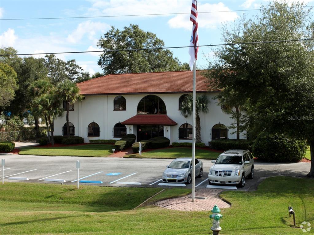 A two-story white commercial building with a red tile roof and a front parking lot — 7725 N ORANGE BLOSSOM TRAIL, ORLANDO, FL