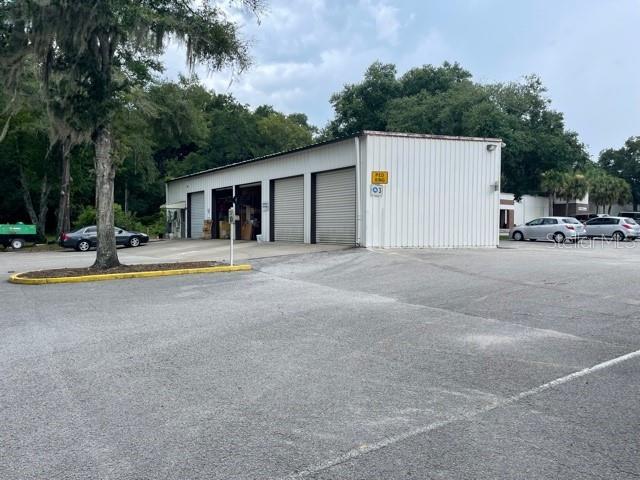 A white metal warehouse building with multiple roll-up doors sits in a paved parking lot — 7725 N ORANGE BLOSSOM TRAIL, ORLANDO, FL