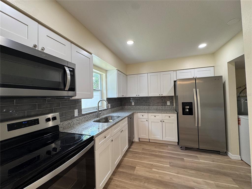 A kitchen features white cabinets, granite countertops, stainless steel appliances, and a gray tile backsplash — 665 W JUNIATA STREET, CLERMONT, FL