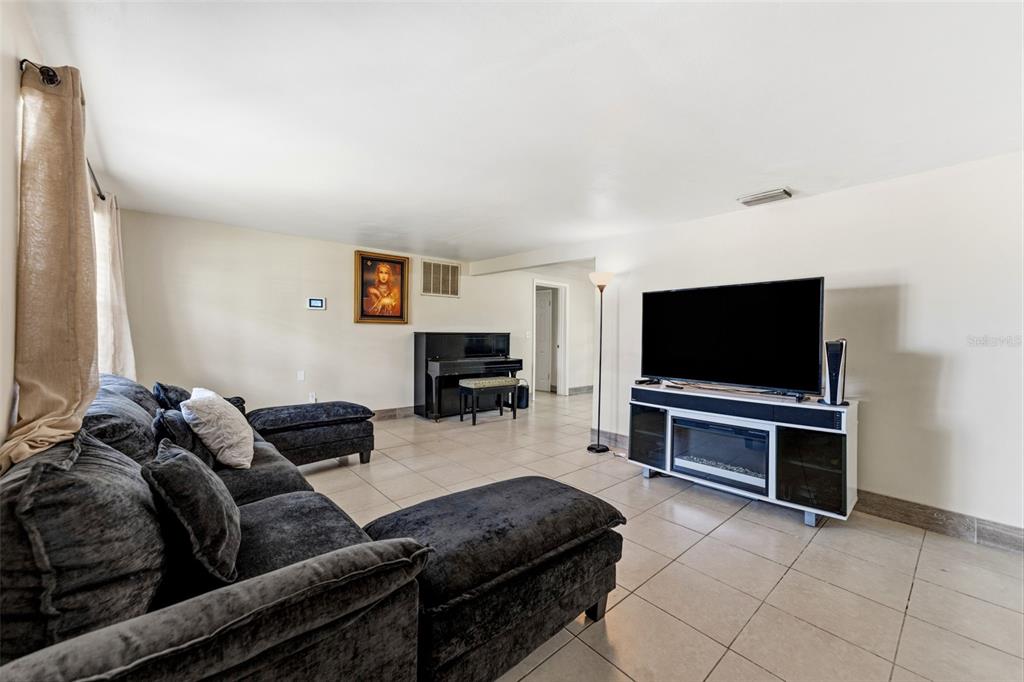 A living room features a dark sectional sofa, a piano, and a television on a stand — 3849 LUMA DRIVE, HOLIDAY, FL