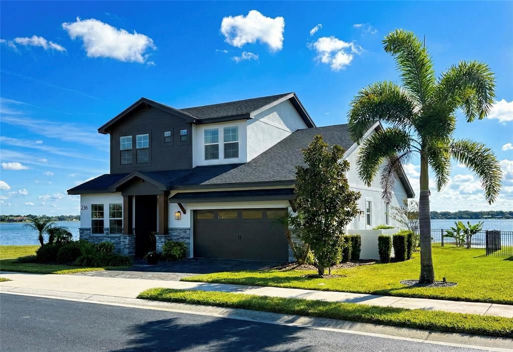 A two-story house with a garage and palm tree sits along a waterfront property — 236 CALADIUM AVENUE, LAKE ALFRED, FL