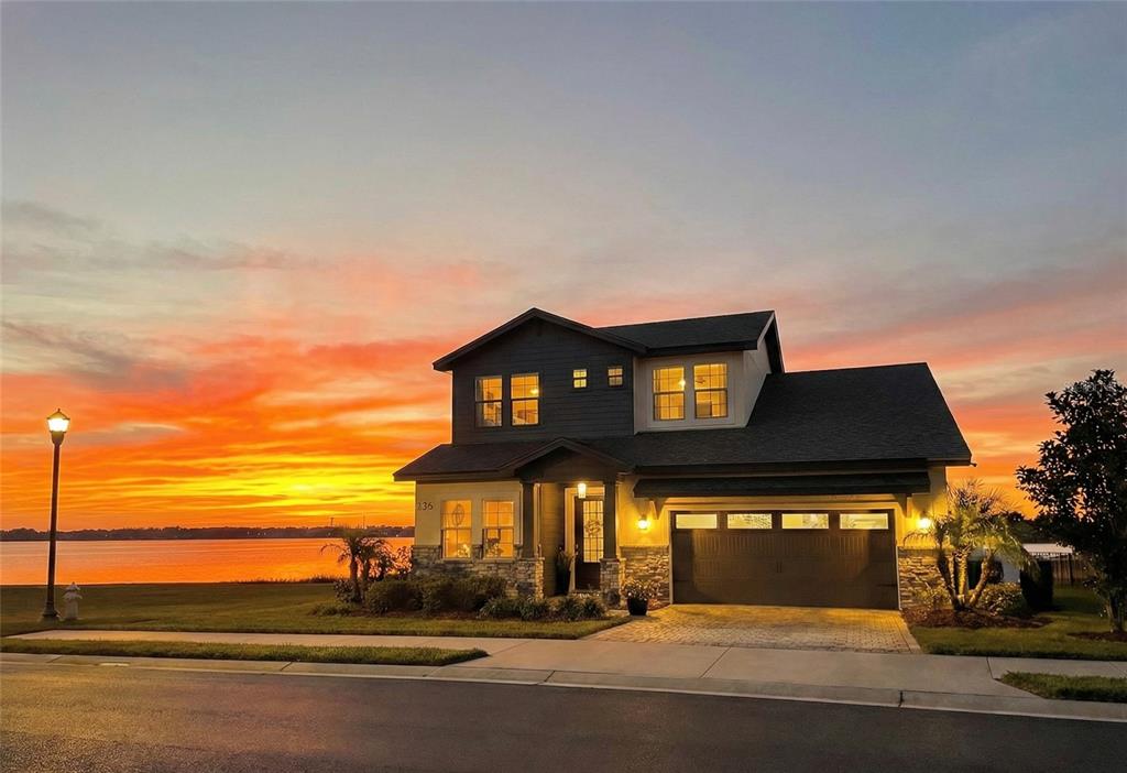 A two-story house with a garage and stone accents sits by a lake at sunset — 236 CALADIUM AVENUE, LAKE ALFRED, FL