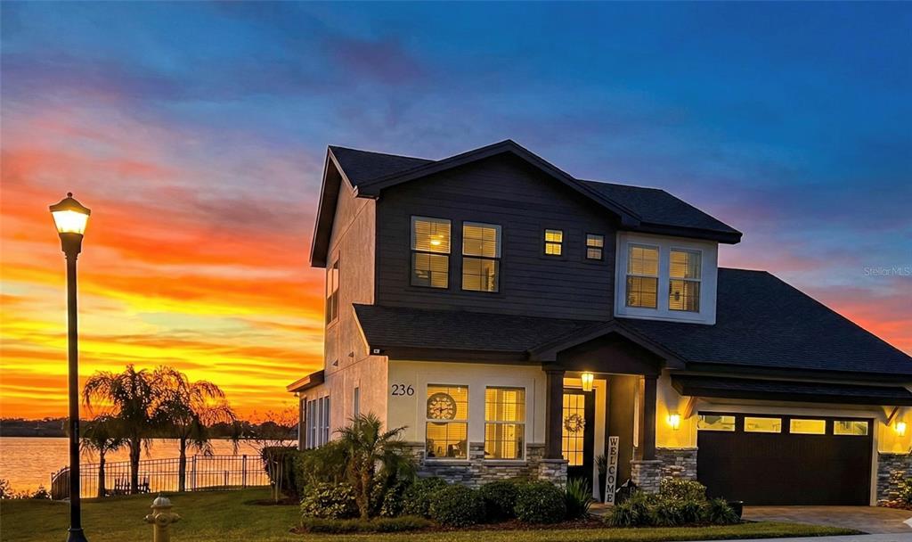 A two-story house with dark siding and stone accents sits by a lake at sunset — 236 CALADIUM AVENUE, LAKE ALFRED, FL