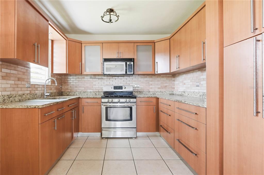 A kitchen with light wood cabinets, stainless steel appliances, granite countertops, and a tiled backsplash — 831 SECTOR LOS TORRES BO. MINILLAS UNIT 5.2, BAYAMON, PR