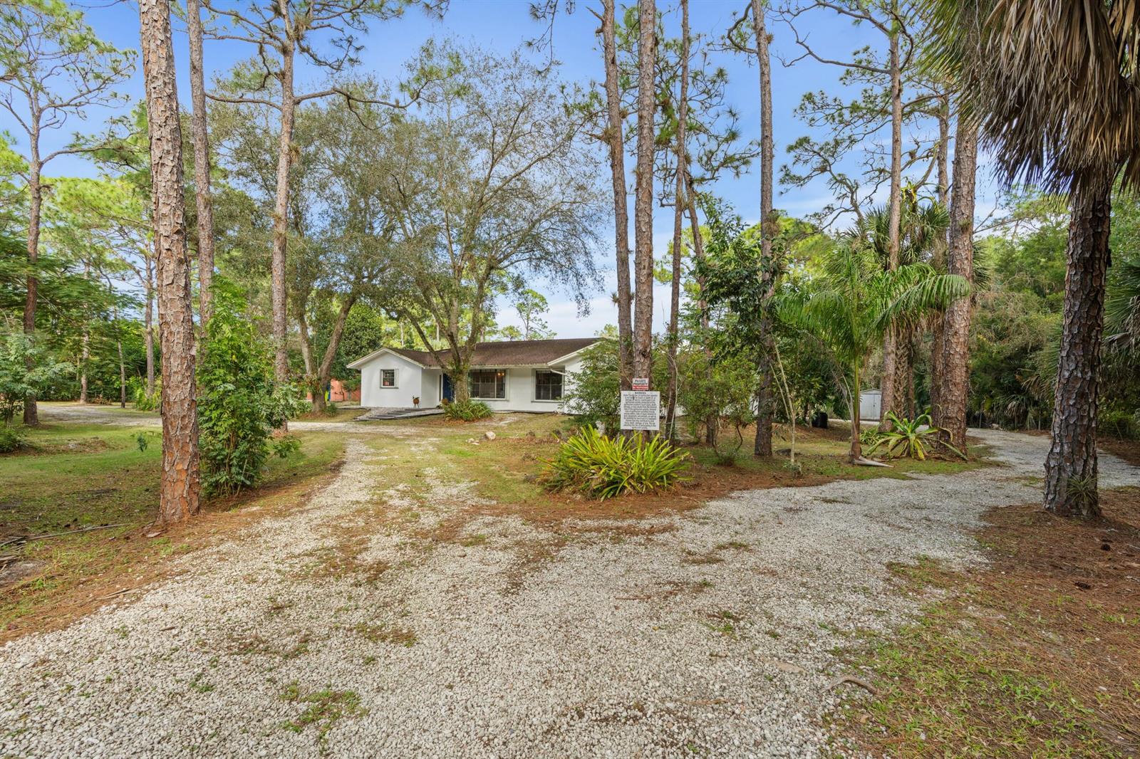 A white single-story house sits at the end of a gravel driveway surrounded by trees — 14817 Snail Trail, FL 33470, FL