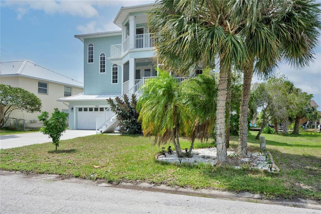 A three-story light blue house with a white garage and palm trees in the front yard — 7352 GULF WAY, HUDSON, FL