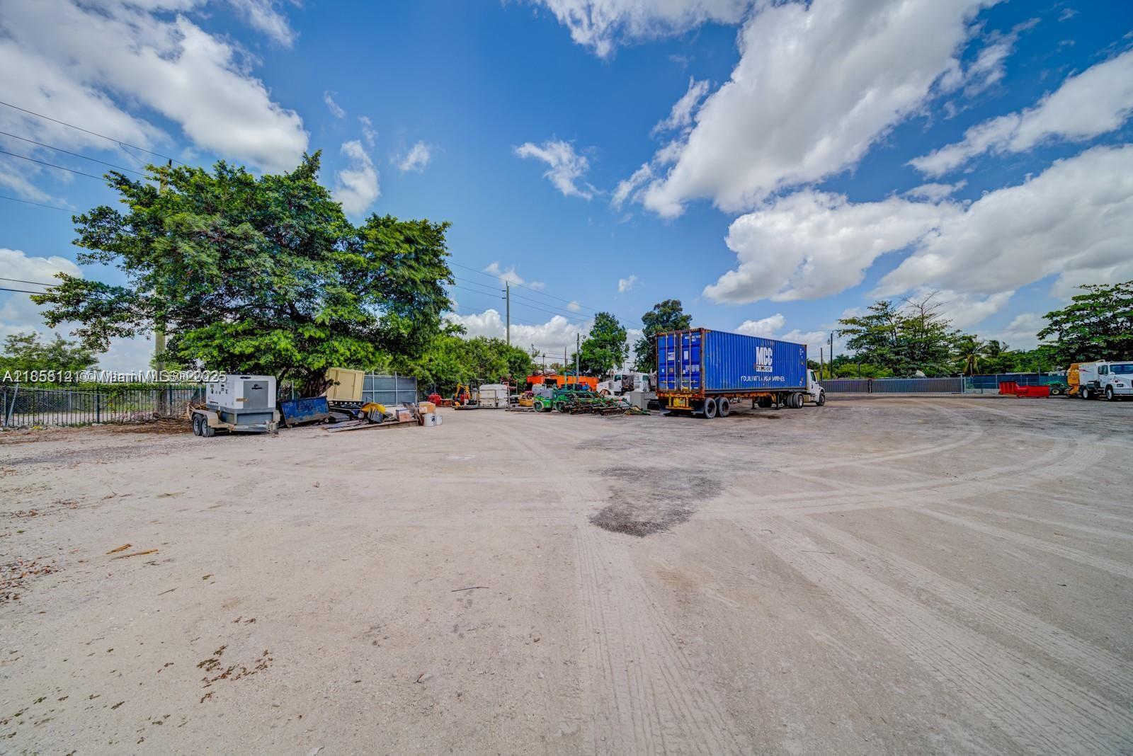 An outdoor storage lot features a blue shipping container, construction equipment, and a large tree — 12160 NW 157 st, Miami FL 33018, MIAMI, FL
