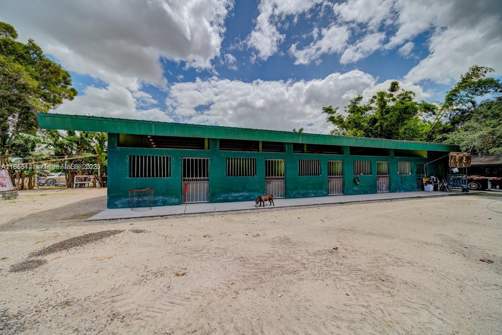 A long, green, single-story stable building with multiple stalls stands on a dirt lot — 12160 NW 157 st, Miami FL 33018, MIAMI, FL