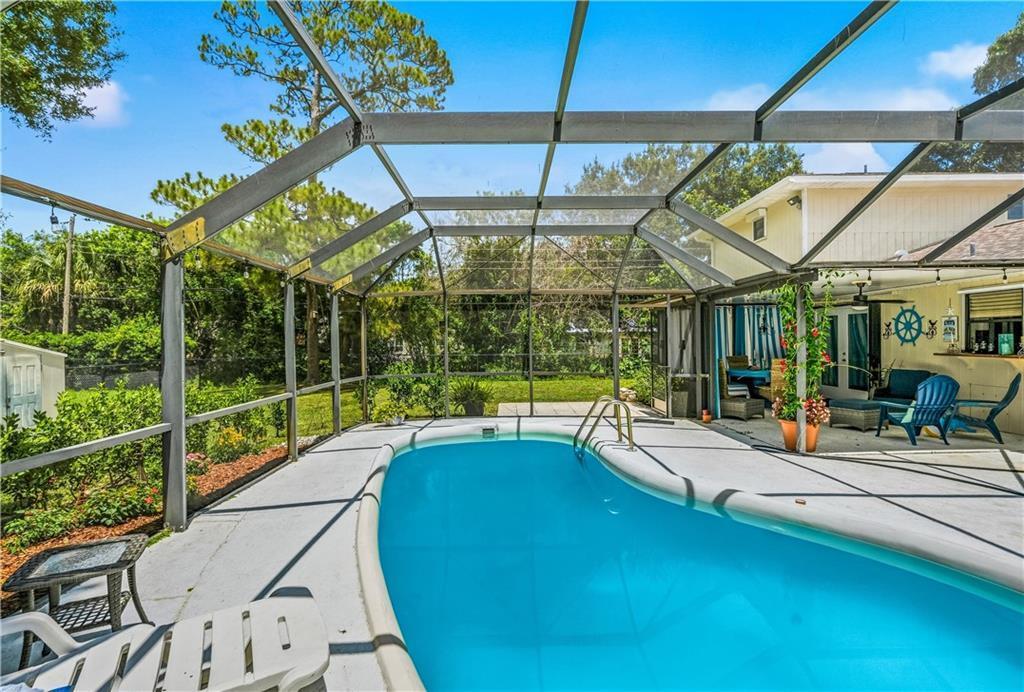 A screened-in backyard pool area with a concrete deck and patio furniture — VERO BEACH, FL