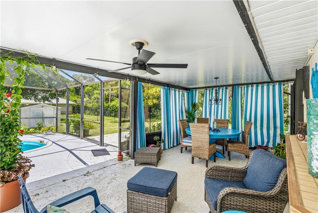 A screened-in patio features a dining set, wicker furniture, blue curtains, and a ceiling fan — VERO BEACH, FL