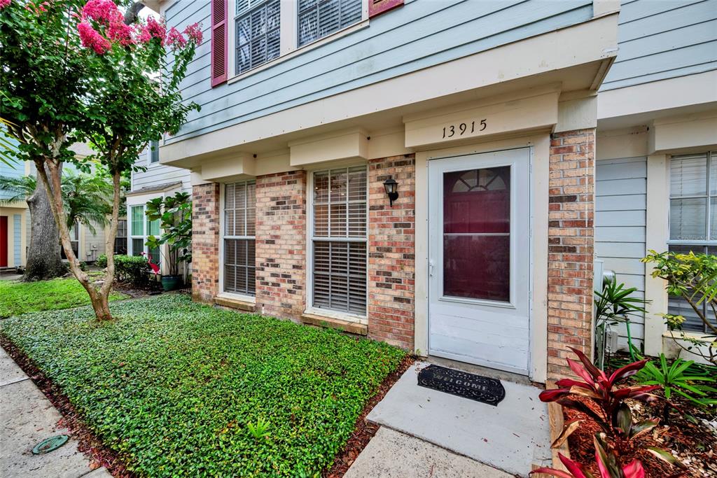 A two-story townhouse exterior features brick siding, a white front door, and a landscaped yard — 13915 FLETCHERS MILL DRIVE, TAMPA, FL