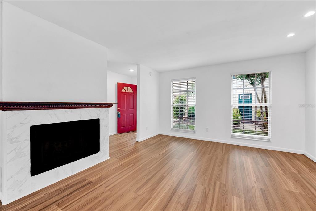 A living room with wood-look flooring, a marble-faced fireplace, and a red front door — 13915 FLETCHERS MILL DRIVE, TAMPA, FL