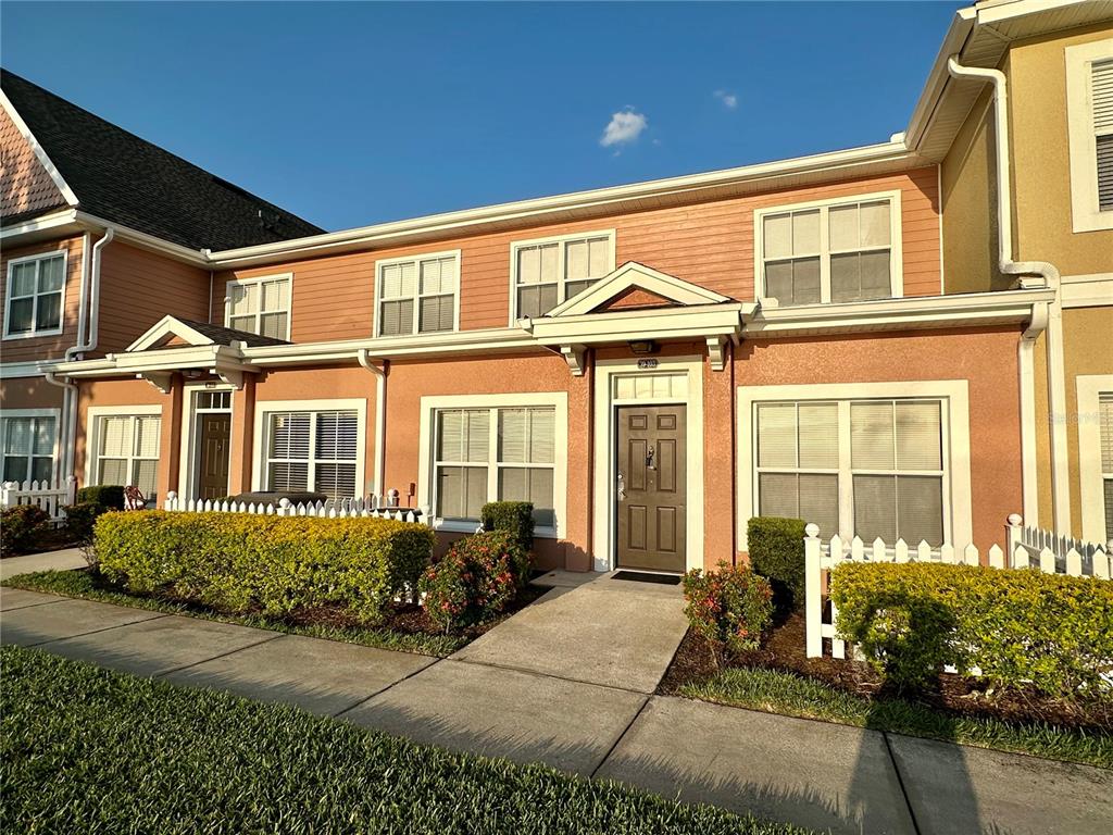 A two-story townhouse exterior features peach-colored siding, white trim, and a small white picket fence — 2200 SAN VITTORINO CIRCLE UNIT 103, KISSIMMEE, FL