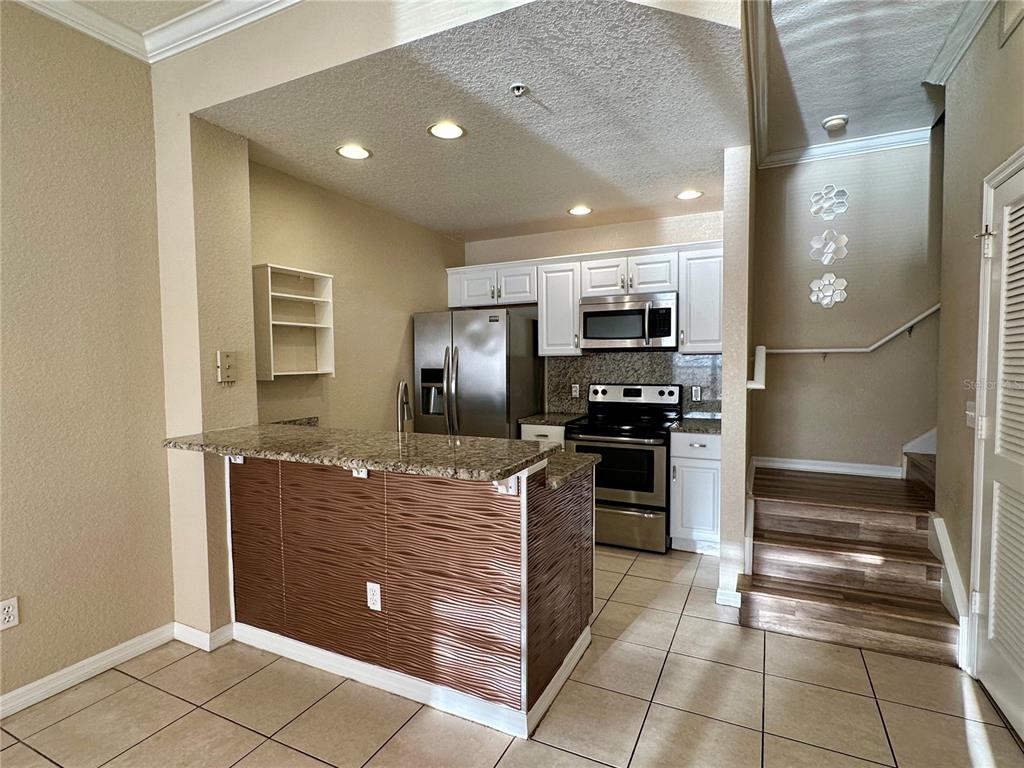 A kitchen features granite countertops, stainless steel appliances, white cabinets, and a textured breakfast bar — 2200 SAN VITTORINO CIRCLE UNIT 103, KISSIMMEE, FL