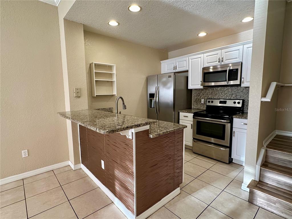 A kitchen features granite countertops, stainless steel appliances, white cabinets, and a textured wood-paneled island — 2200 SAN VITTORINO CIRCLE UNIT 103, KISSIMMEE, FL