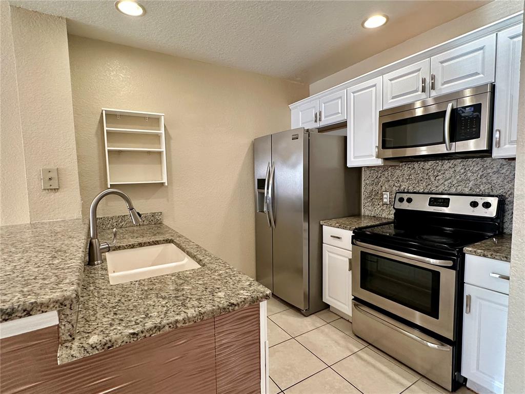 A kitchen features stainless steel appliances, white cabinets, and granite countertops — 2200 SAN VITTORINO CIRCLE UNIT 103, KISSIMMEE, FL