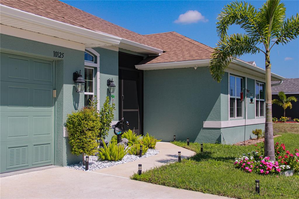 A teal-colored house exterior features a garage, a front entryway, and a palm tree — 10125 AUDREY STREET, PORT CHARLOTTE, FL