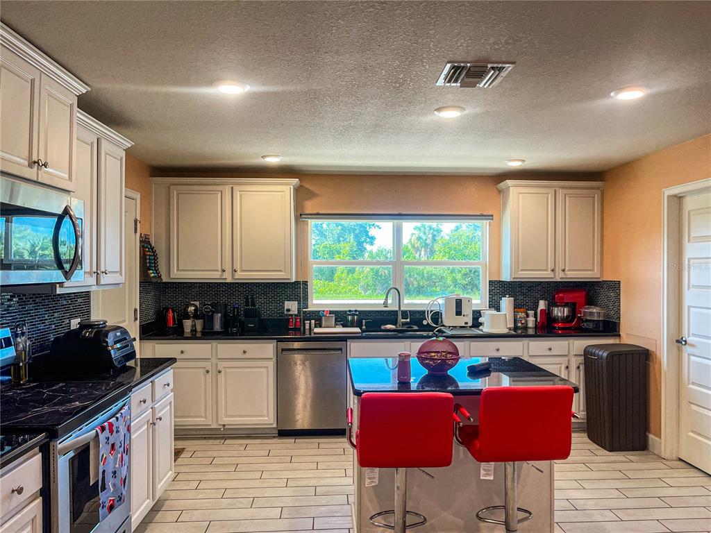 A kitchen features white cabinets, black countertops, a central island with red stools, and tile flooring — 10125 AUDREY STREET, PORT CHARLOTTE, FL