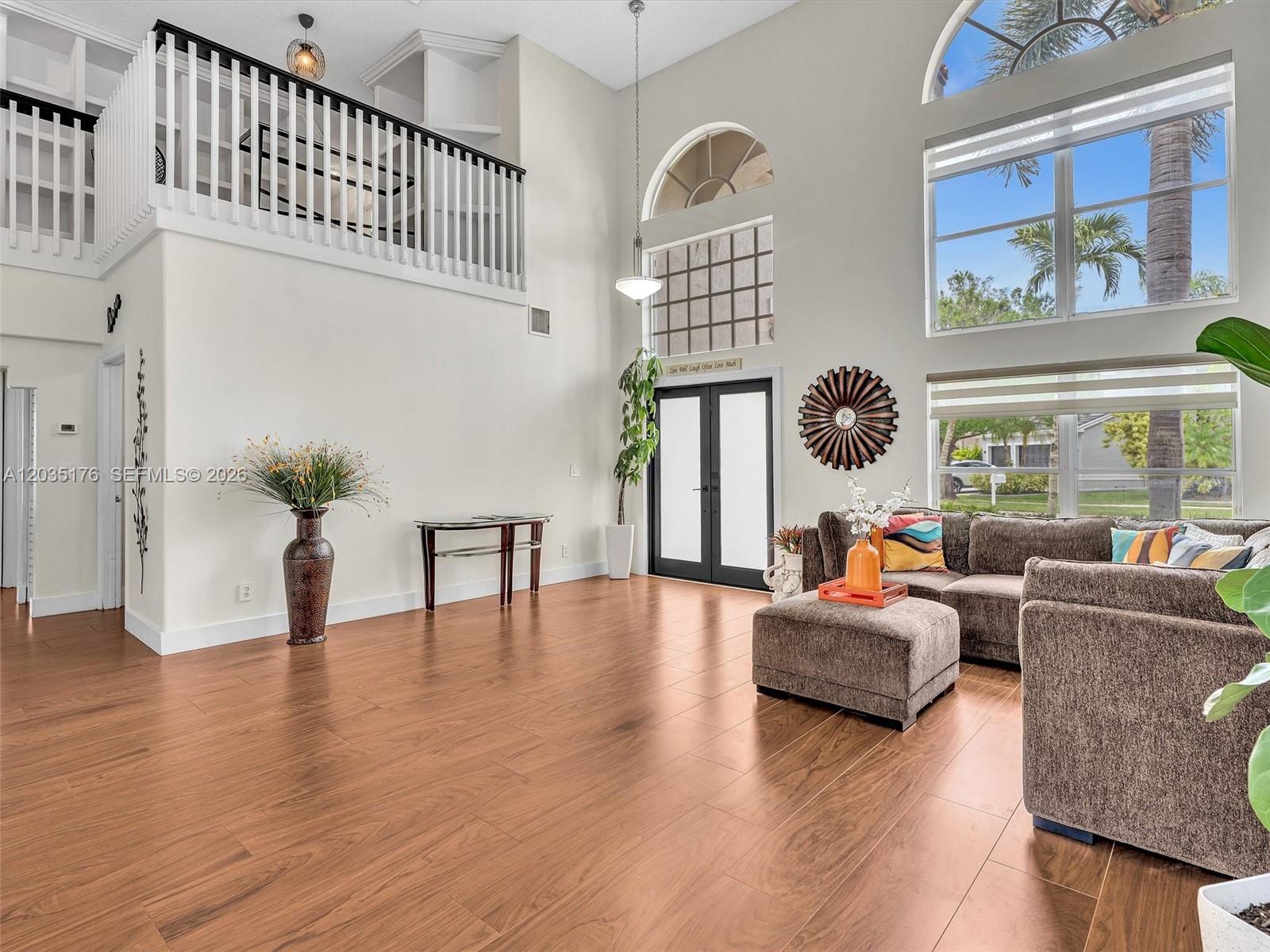 A spacious living room features high ceilings, wood-look flooring, a loft balcony, and large windows — 2654 SW 181st Ter, Miramar FL 33029, MIRAMAR, FL