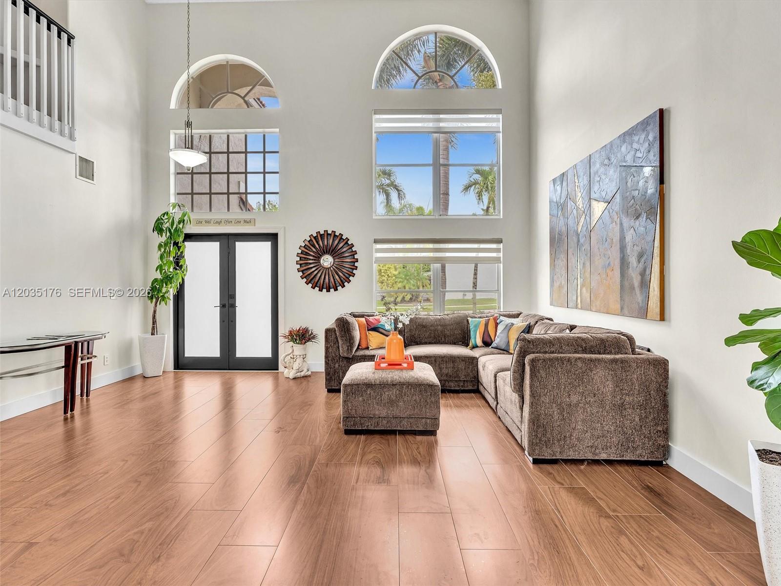 A high-ceilinged living room features wood-look flooring, a large sectional sofa, and tall windows — 2654 SW 181st Ter, Miramar FL 33029, MIRAMAR, FL