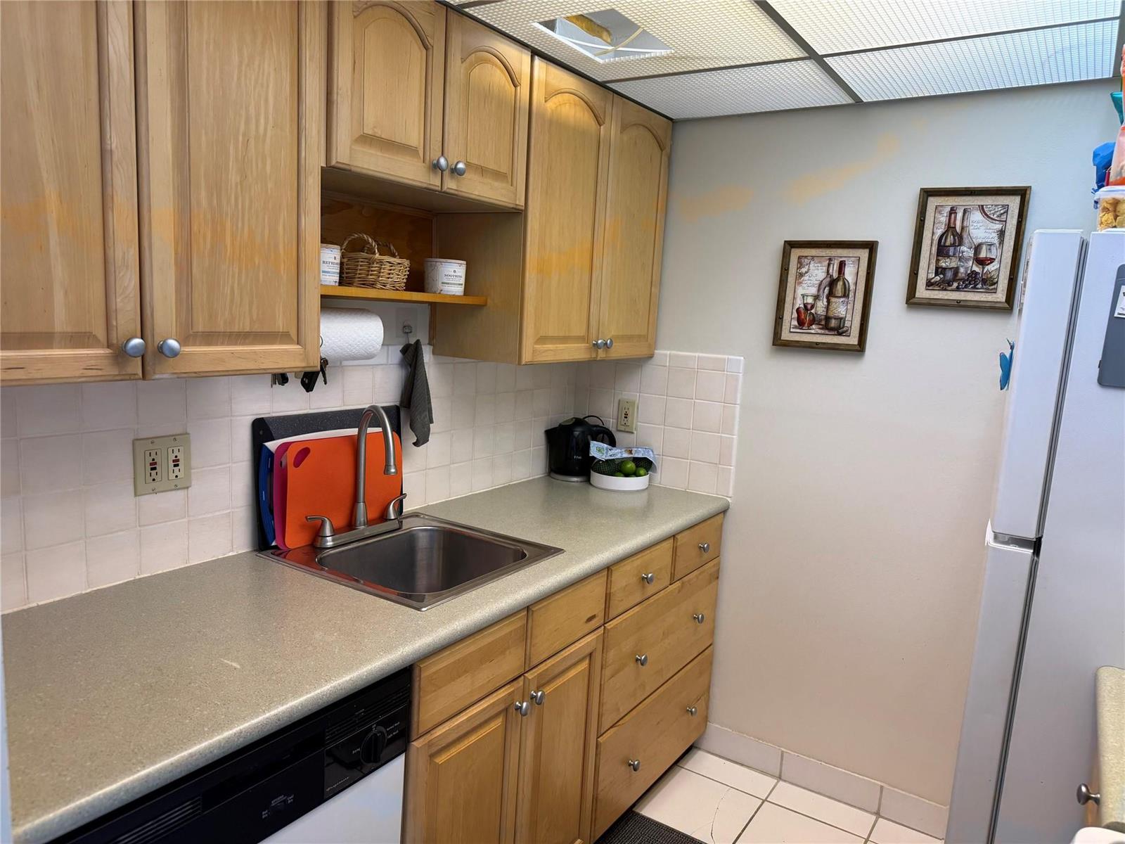 A kitchen features light wood cabinets, a stainless steel sink, and white tiled backsplashes — 111 Briny Avenue # 1909, Pompano Beach FL 33062, POMPANO BEACH, FL