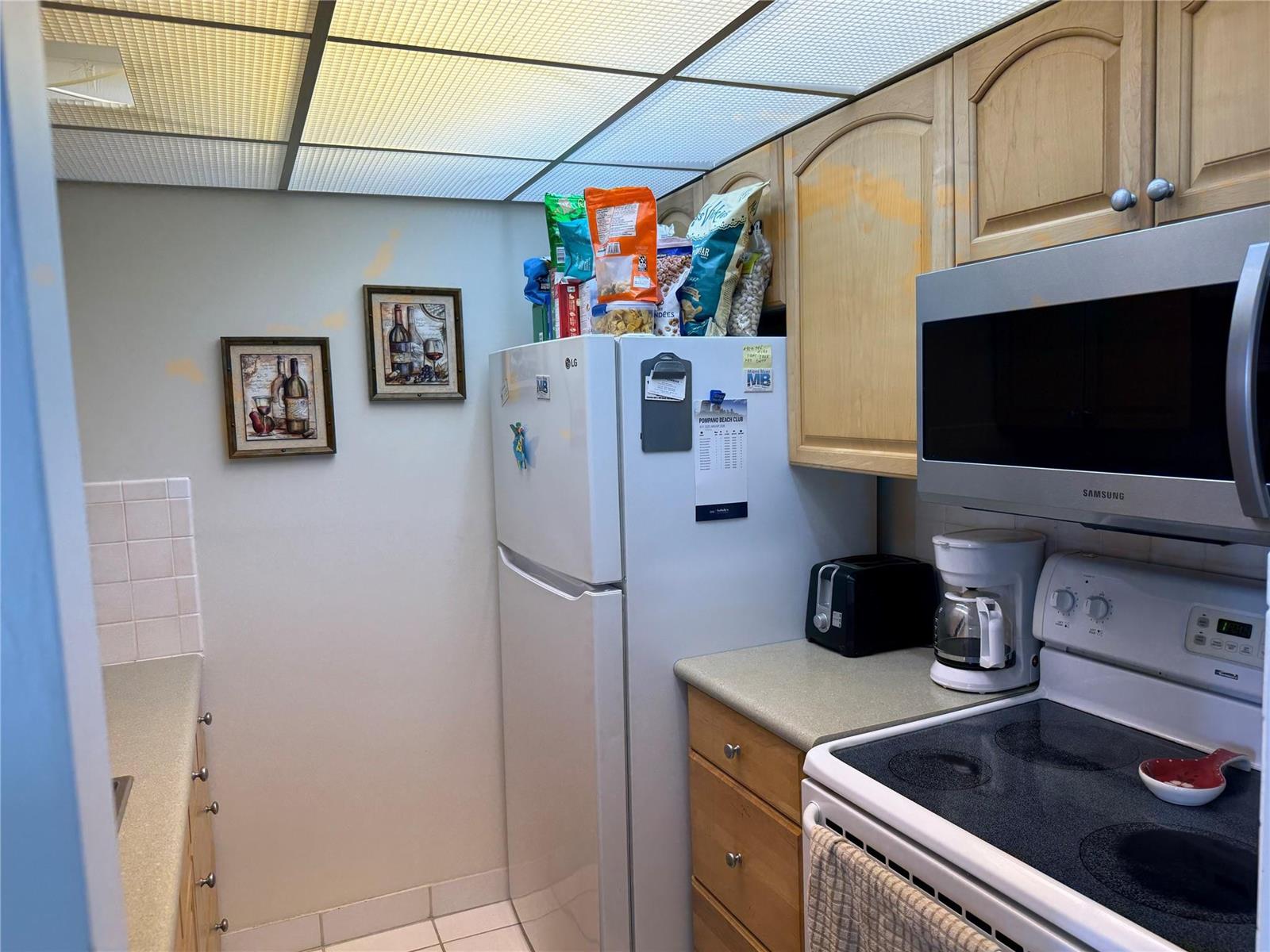 A kitchen features light wood cabinets, white appliances, a drop ceiling, and a tiled floor — 111 Briny Avenue # 1909, Pompano Beach FL 33062, POMPANO BEACH, FL