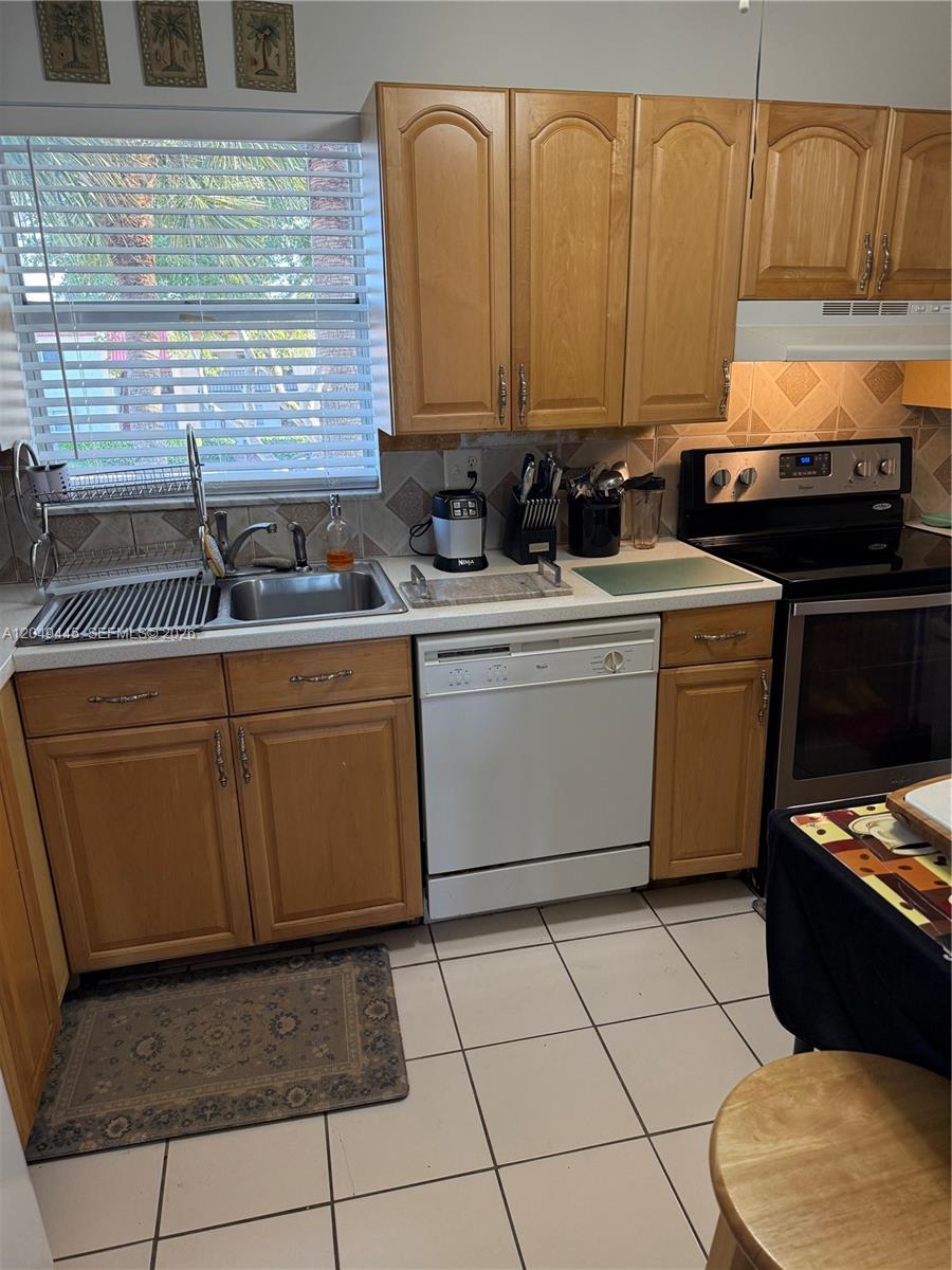 A kitchen features light wood cabinets, white appliances, a tiled backsplash, and a window — WEST PALM BEACH, FL