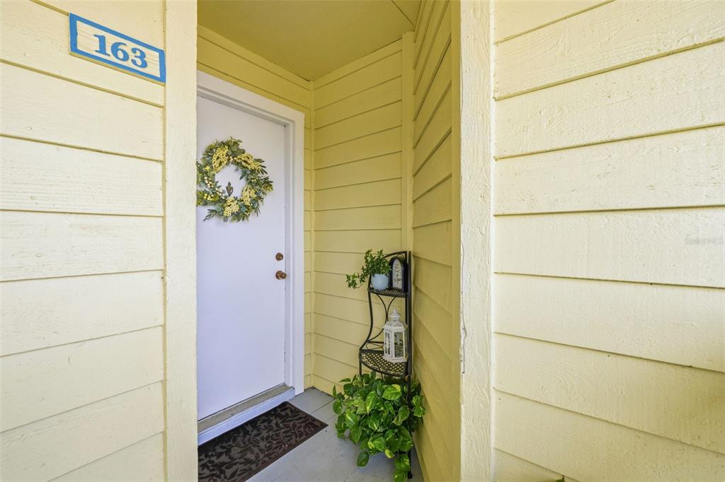 A white front door with a wreath is set in a yellow-sided exterior entryway — 455 ALT 19 S UNIT 163, PALM HARBOR, FL