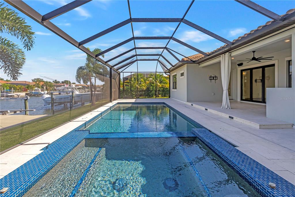 A screened-in pool and spa overlook a canal with boats in a residential backyard — 513 17TH AVENUE E, PALMETTO, FL
