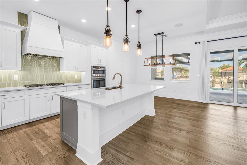 A modern kitchen features white cabinets, a gray island, a tile backsplash, and wood flooring — 513 17TH AVENUE E, PALMETTO, FL